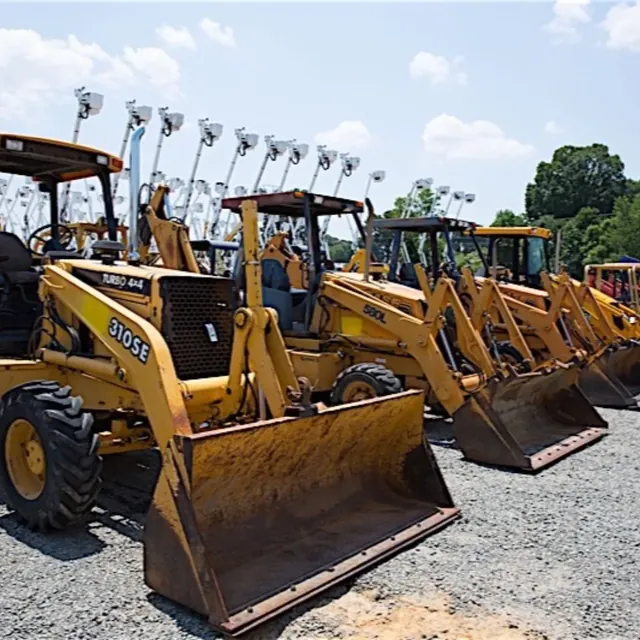 Row of backhoe loaders with bucket trucks behind in an equipment yard