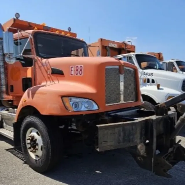 Kenworth dump truck with a plow hitch beside other municipal trucks