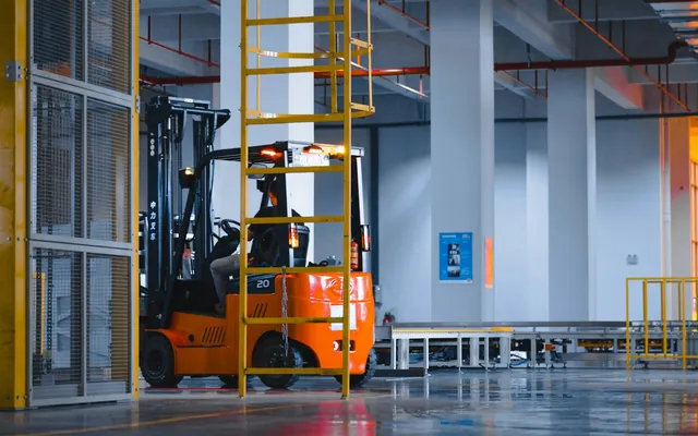 Orange electric forklift in a plant bay seen from behind